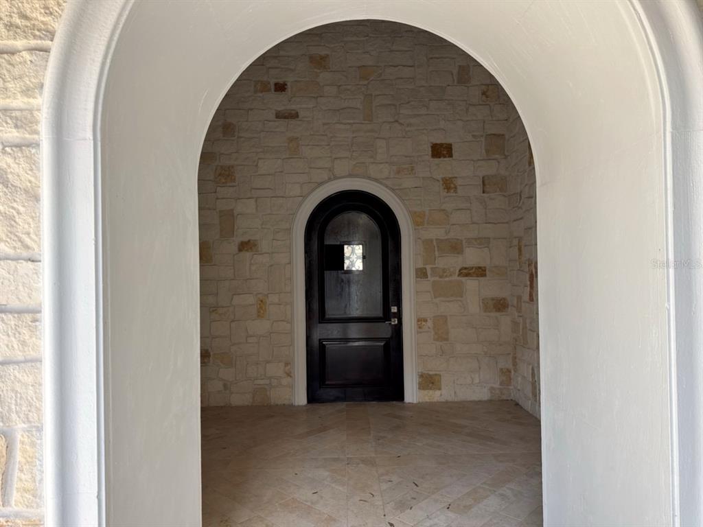 A dark arched front door is set within a stone-walled entryway under a large archway — 9003 WATERASH LANE N, PINELLAS PARK, FL