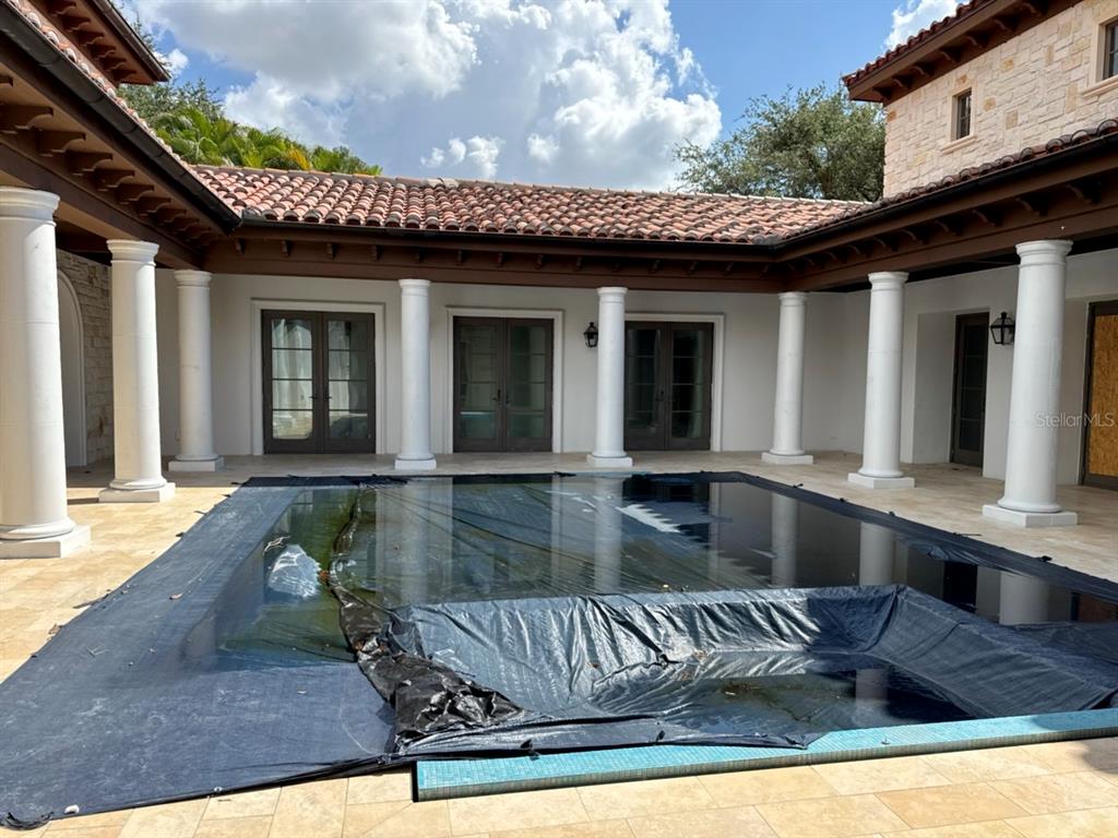 A covered swimming pool sits in a courtyard surrounded by white columns and a tiled roof — 9003 WATERASH LANE N, PINELLAS PARK, FL