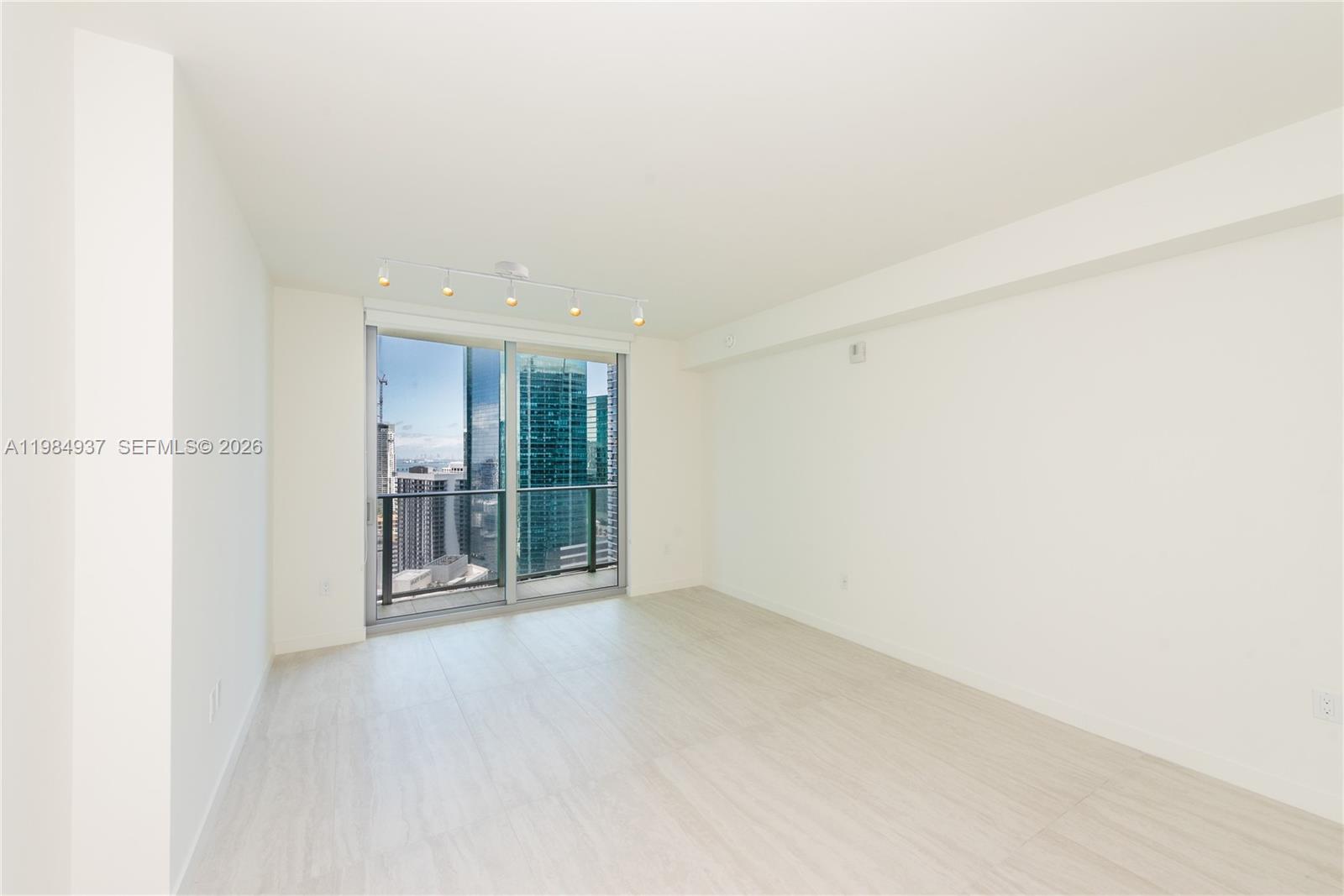 An empty room features white walls, light wood-look flooring, and a sliding glass balcony door — 77 SE 5th Street # 4004, Miami FL 33131, MIAMI, FL
