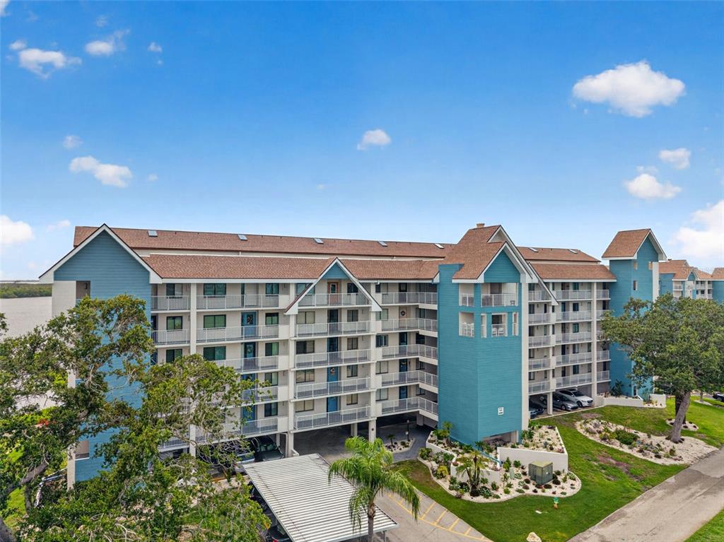 An exterior view of a multi-story blue apartment building with balconies and a parking area — 4650 BAY BOULEVARD UNIT 1044, PORT RICHEY, FL