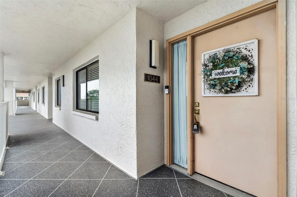 An exterior view of a building hallway featuring a beige door with a welcome wreath — 4650 BAY BOULEVARD UNIT 1044, PORT RICHEY, FL