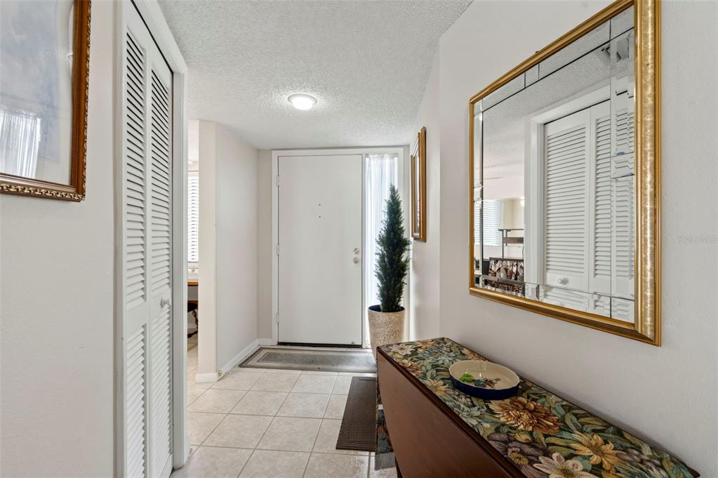 An entryway features a white front door, tiled flooring, a console table, and a wall mirror — 4650 BAY BOULEVARD UNIT 1044, PORT RICHEY, FL