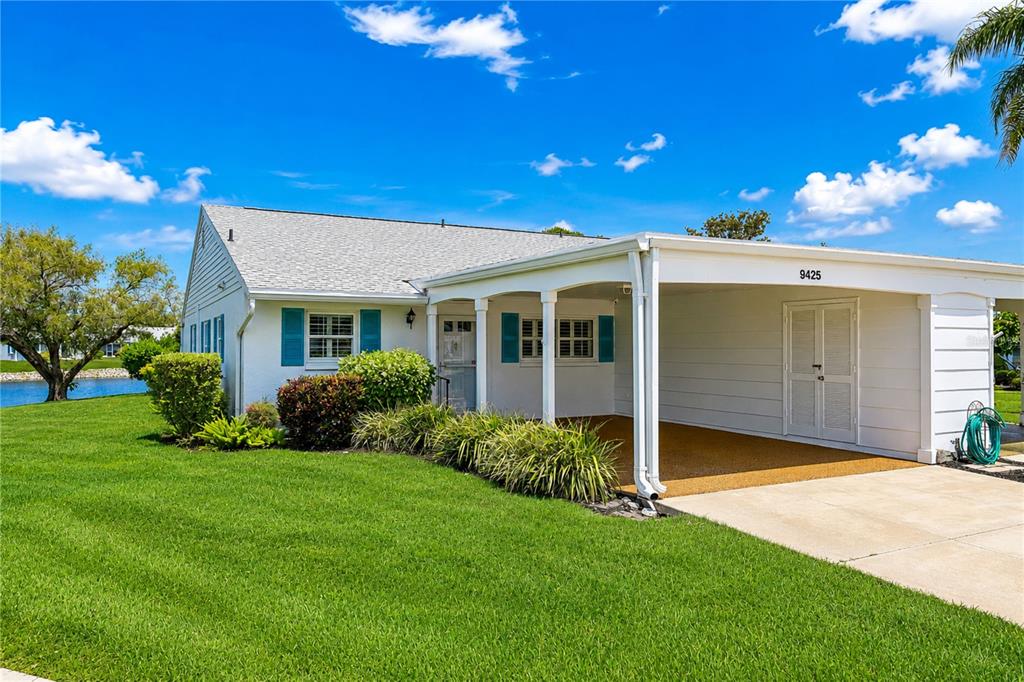 A white single-story house features a covered carport, blue shutters, and a green lawn — 9425 ANDOVER CIRCLE, BRADENTON, FL