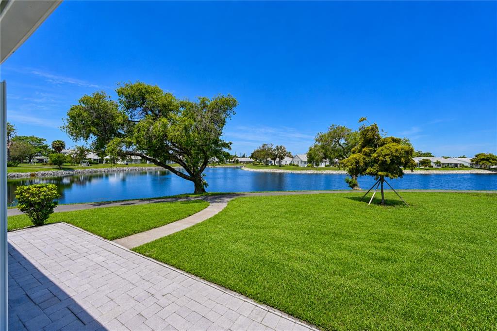 A paved patio overlooks a grassy lawn, a small lake, and distant residential buildings — 9425 ANDOVER CIRCLE, BRADENTON, FL