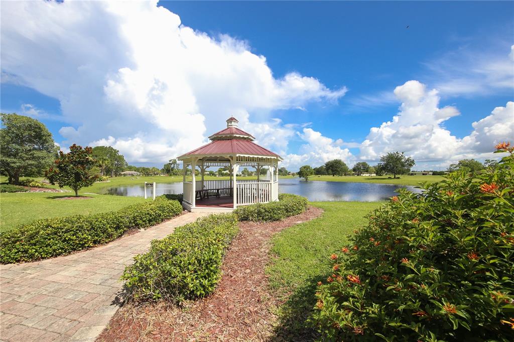 A white gazebo sits on a brick path beside a pond under a cloudy sky — 16216 QUESA DRIVE, PUNTA GORDA, FL
