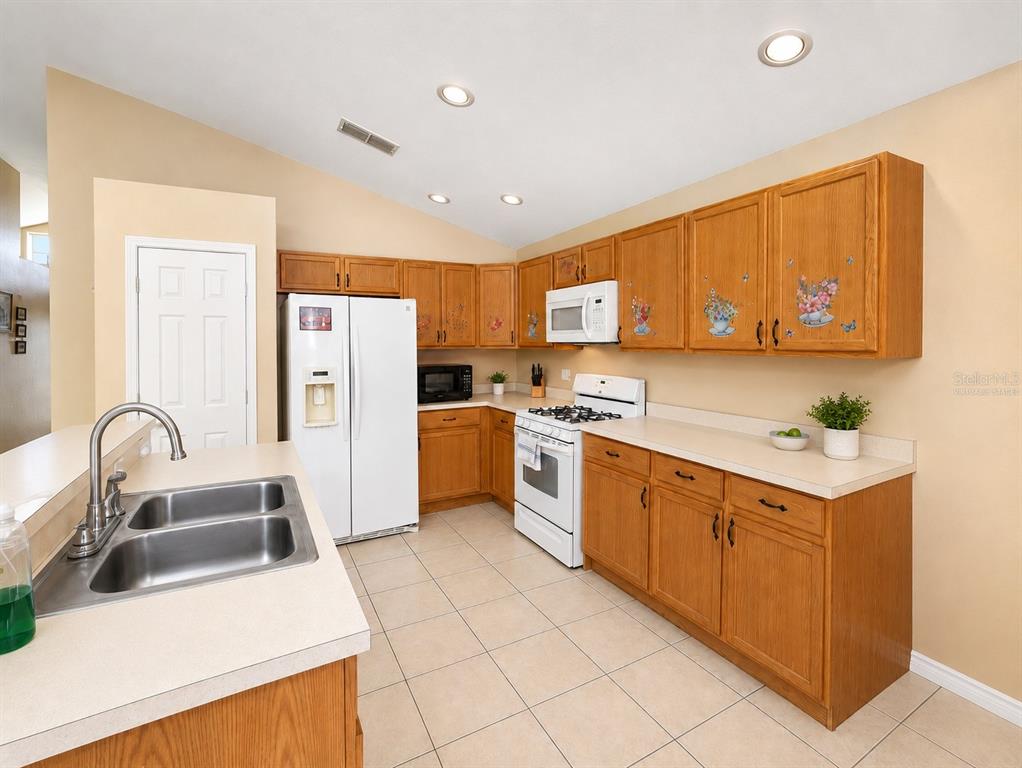 A kitchen features oak cabinets, white appliances, a double sink, and light-colored tile flooring — 531 SILVER PALMS CIRCLE, DAVENPORT, FL