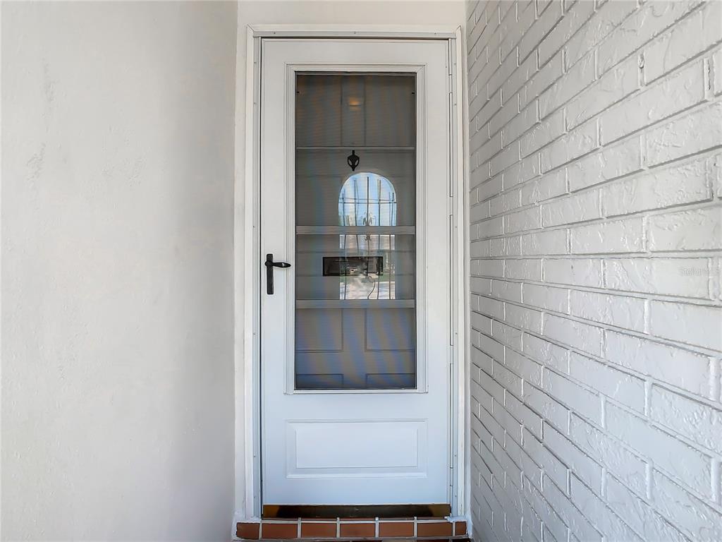 A white storm door is installed in a doorway between a smooth wall and a brick wall — 4230 REDCLIFF PLACE UNIT 4230, NEW PORT RICHEY, FL