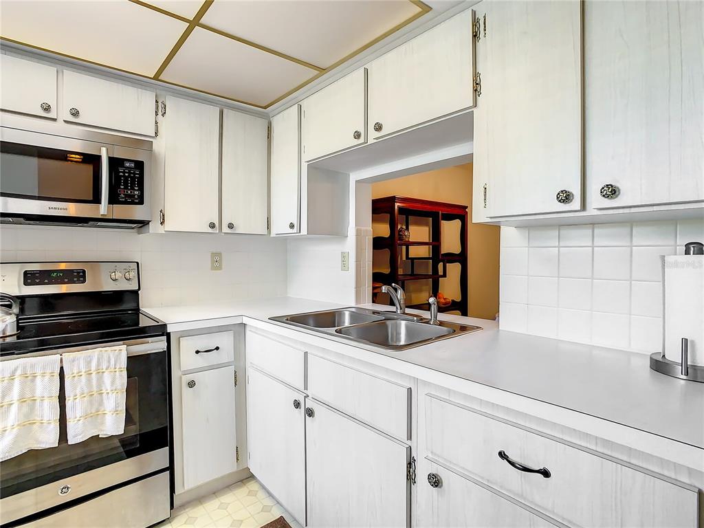 A kitchen features white cabinets, stainless steel appliances, a double sink, and white tile backsplash — 4230 REDCLIFF PLACE UNIT 4230, NEW PORT RICHEY, FL