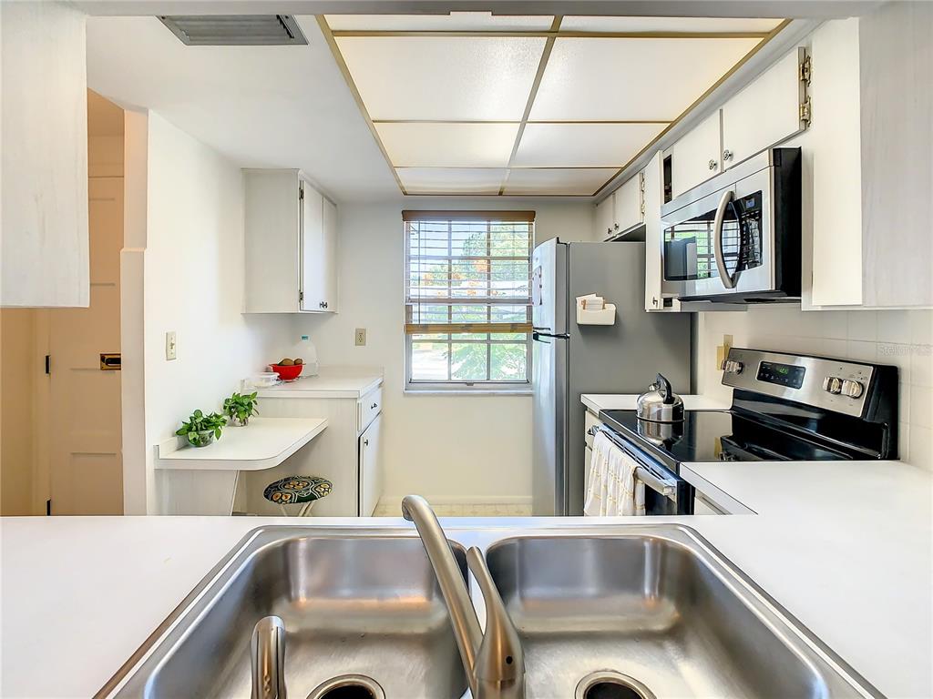 A kitchen features white cabinets, a double-basin sink, stainless steel appliances, and a drop-leaf table — 4230 REDCLIFF PLACE UNIT 4230, NEW PORT RICHEY, FL
