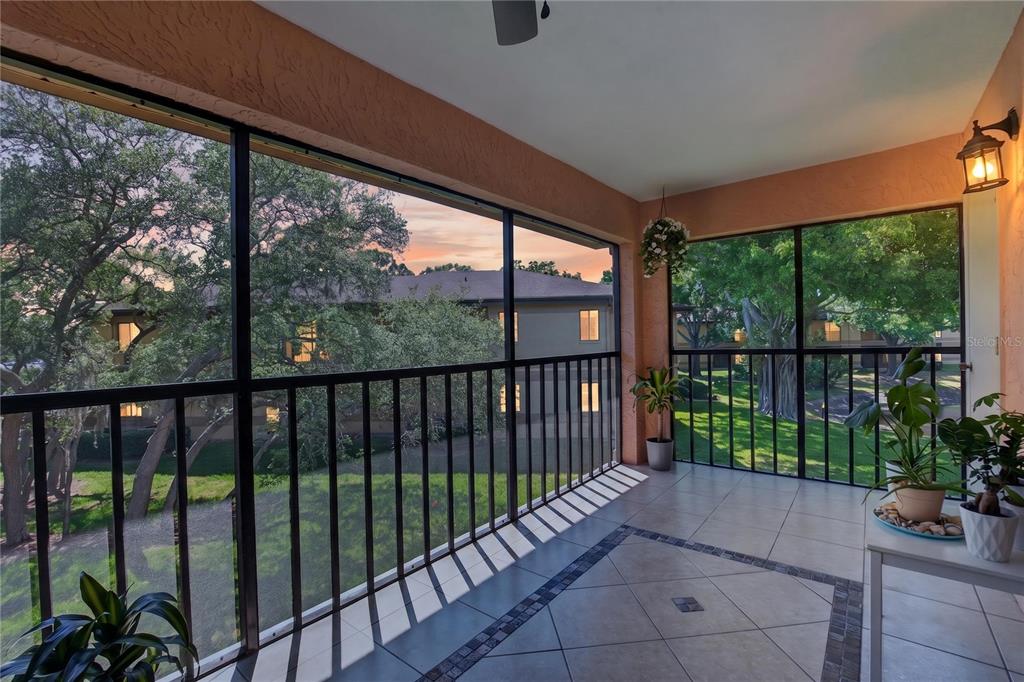 A screened-in balcony with tile flooring, black railings, and views of trees and buildings — 2691 SABAL SPRINGS CIRCLE UNIT 201, CLEARWATER, FL
