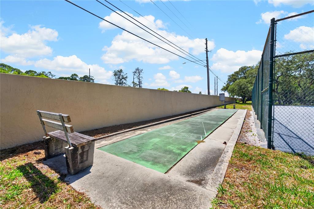 An outdoor shuffleboard court sits next to a tennis court and a concrete wall — 2691 SABAL SPRINGS CIRCLE UNIT 201, CLEARWATER, FL