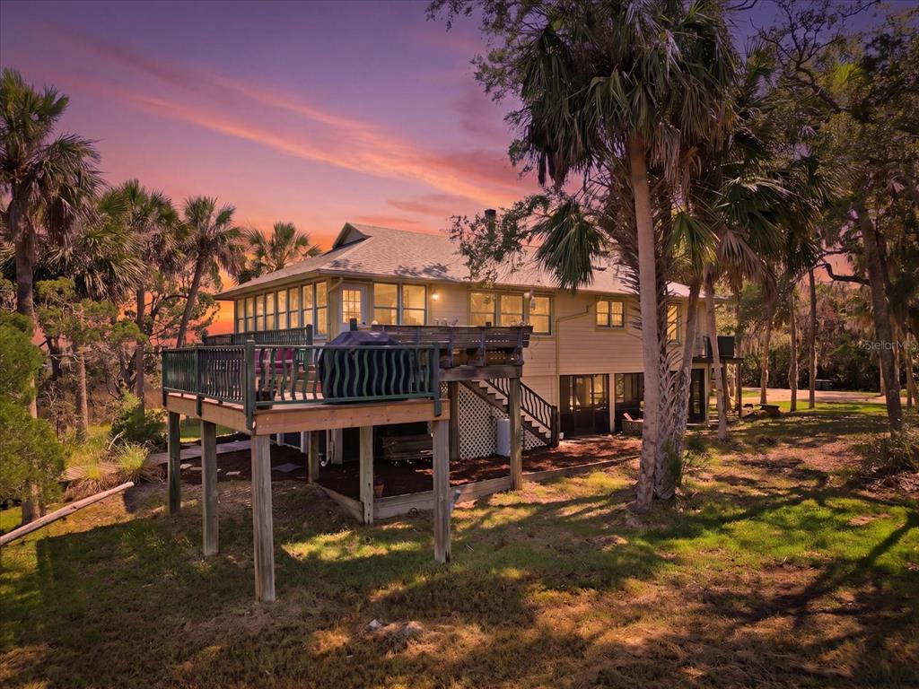 An elevated house with a wooden deck and lattice skirting sits among trees at sunset — 12350 W RED MAPLE STREET, HOMOSASSA, FL