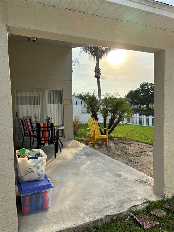 A covered concrete patio features outdoor furniture, a yellow chair, and storage bins — 4304 STONES RIVER COURT, NEW PORT RICHEY, FL