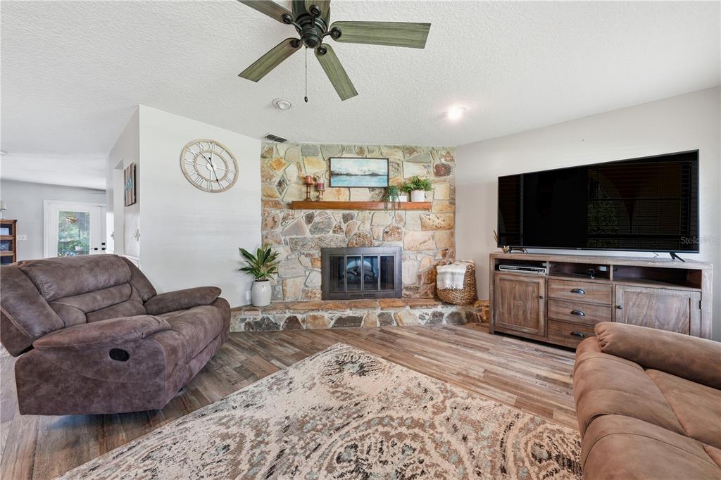 A living room features a stone fireplace, a ceiling fan, and brown furniture — 41300 DIXIE AVENUE, UMATILLA, FL