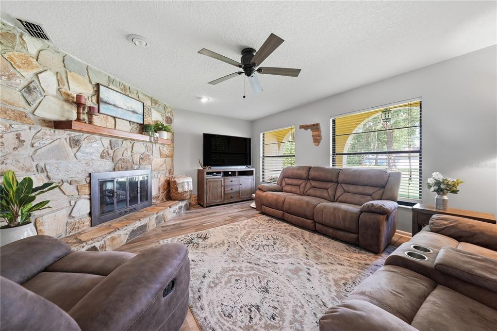 A living room features a stone fireplace, brown reclining furniture, and a ceiling fan — 41300 DIXIE AVENUE, UMATILLA, FL