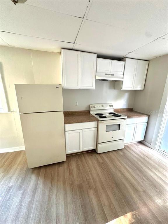 A kitchen features white cabinets, a white refrigerator, a white stove, and wood-look flooring — 404 PENNSYLVANIA AVENUE, CLEARWATER, FL
