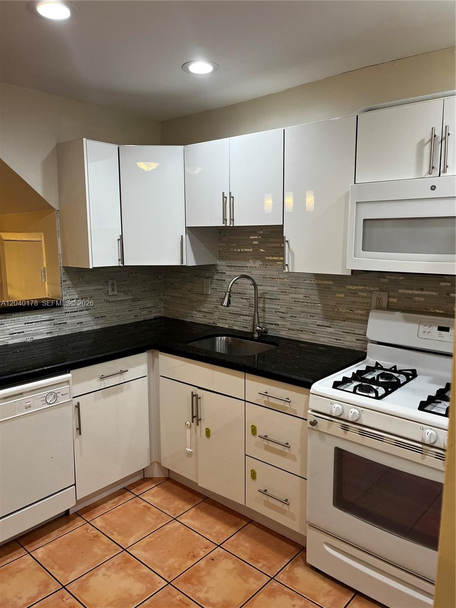 A kitchen features white cabinets, black countertops, a tiled backsplash, and white appliances — 8650 SW 67th Ave # 1029, Pinecrest FL 33156, PINECREST, FL