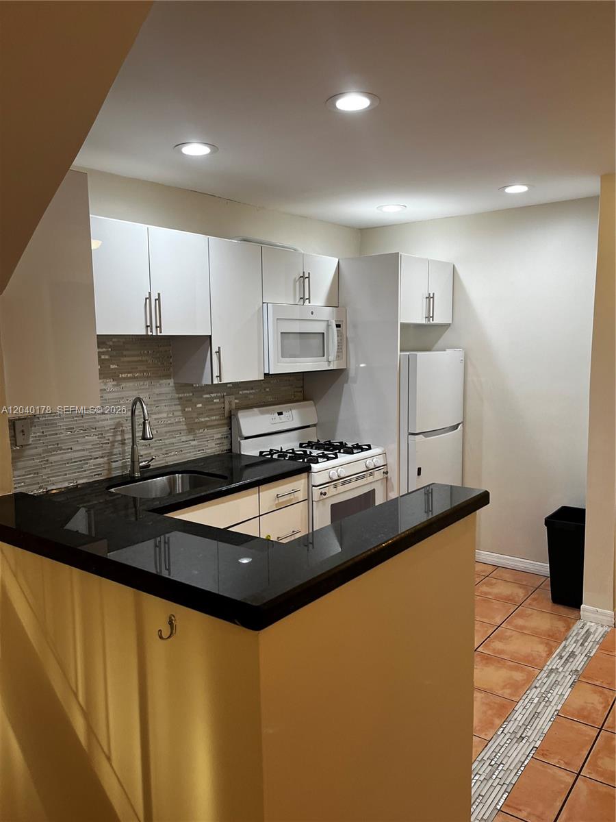 A kitchen features white cabinets, black countertops, a tiled backsplash, and stainless steel appliances — 8650 SW 67th Ave # 1029, Pinecrest FL 33156, PINECREST, FL