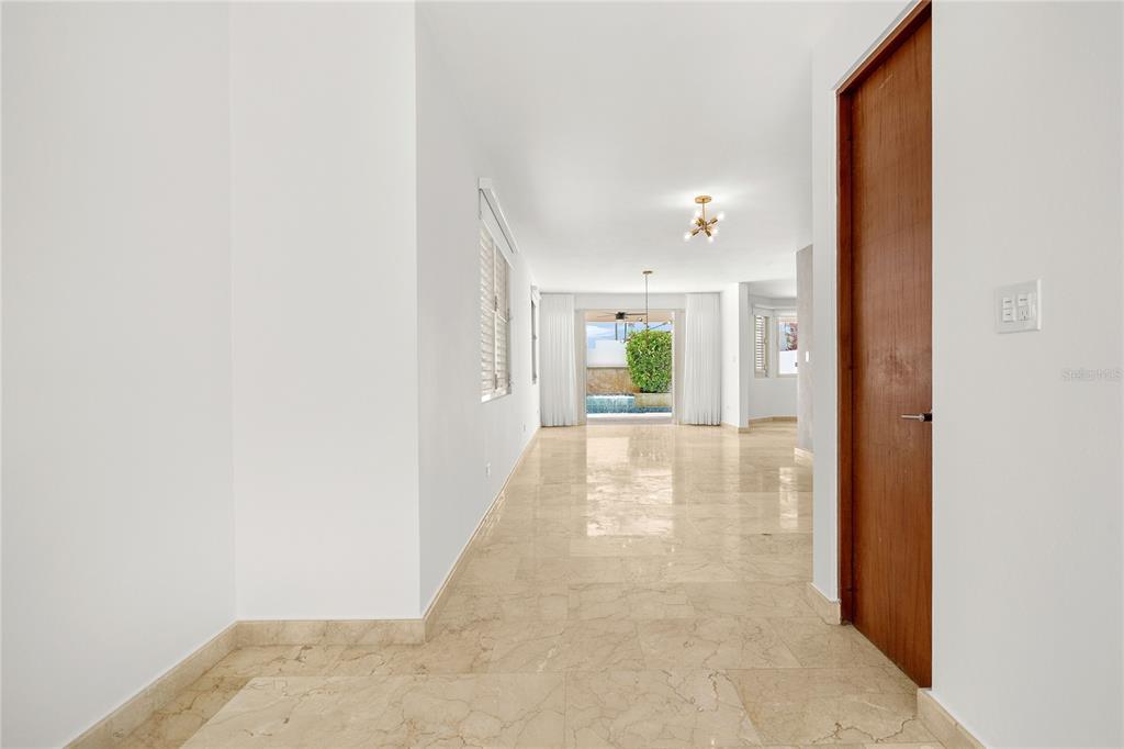 A hallway with marble flooring leads to a living area with a view of a pool — J9 CALLE NATALIA, TRUJILLO ALTO, PR