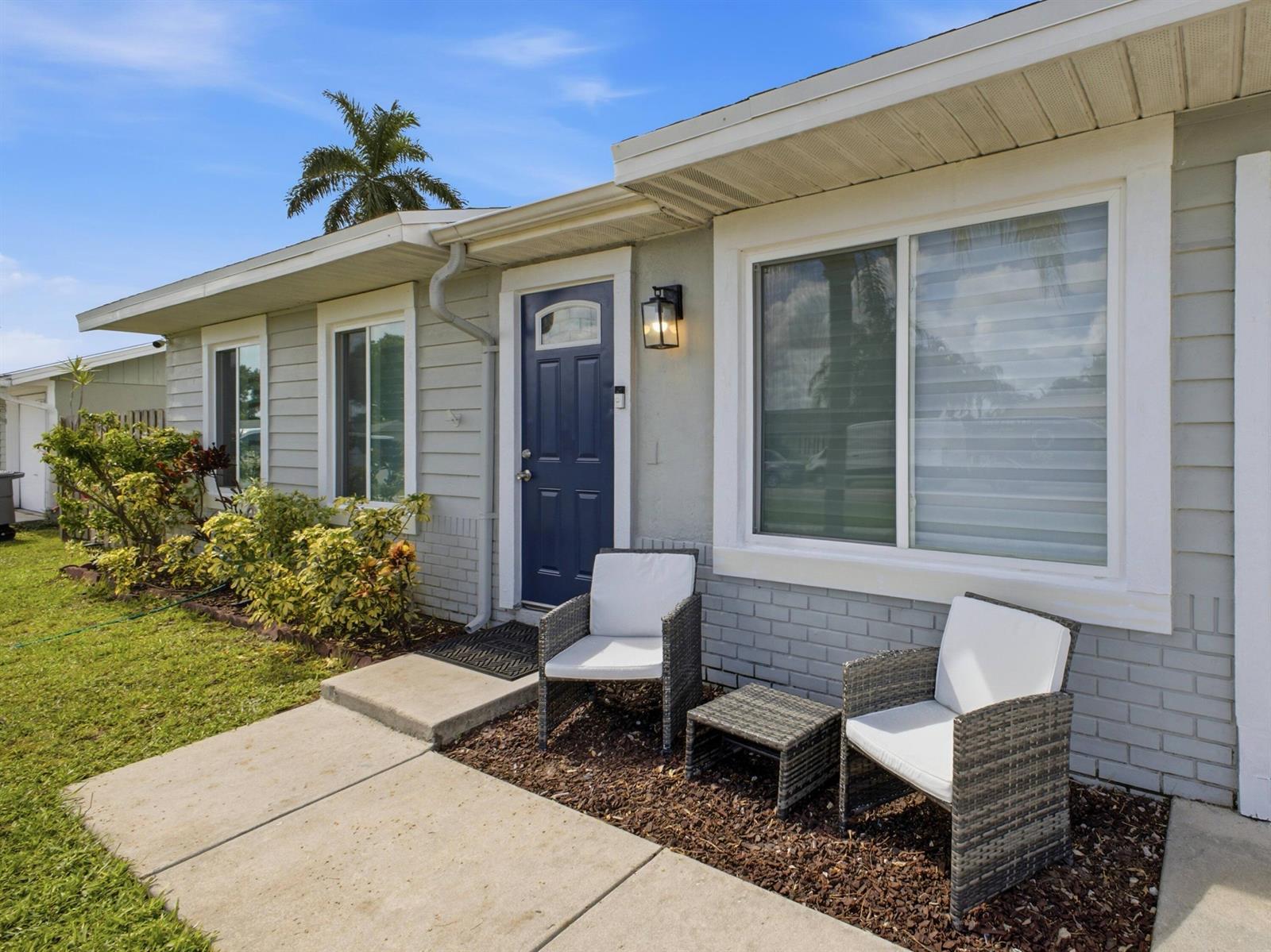 A gray house exterior features a blue front door, two wicker chairs, and a table — 5396 Benjamin Avenue, Boynton Beach FL 33472, BOYNTON BEACH, FL