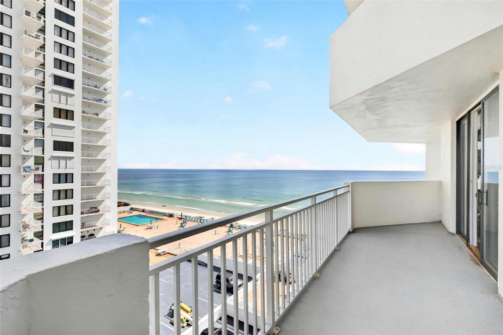 A balcony with white railings overlooks a beach, the ocean, and a neighboring high-rise building — 3047 S ATLANTIC AVENUE UNIT 705, DAYTONA BEACH, FL