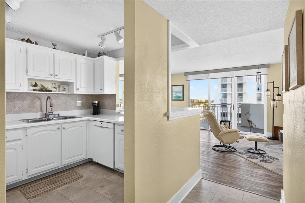 A kitchen with white cabinets and tile floors opens to a living area with balcony access — 3047 S ATLANTIC AVENUE UNIT 705, DAYTONA BEACH, FL