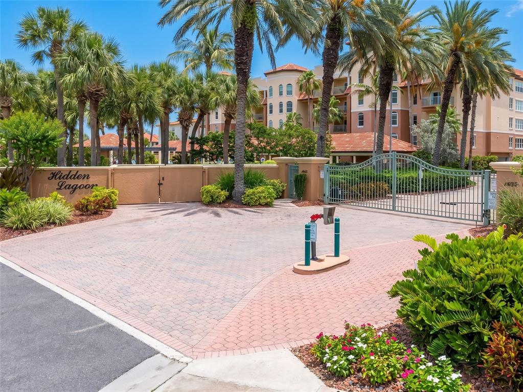 A gated entrance with a paved driveway leads to a multi-story building with palm trees — 1695 PINELLAS BAYWAY S UNIT D1, TIERRA VERDE, FL