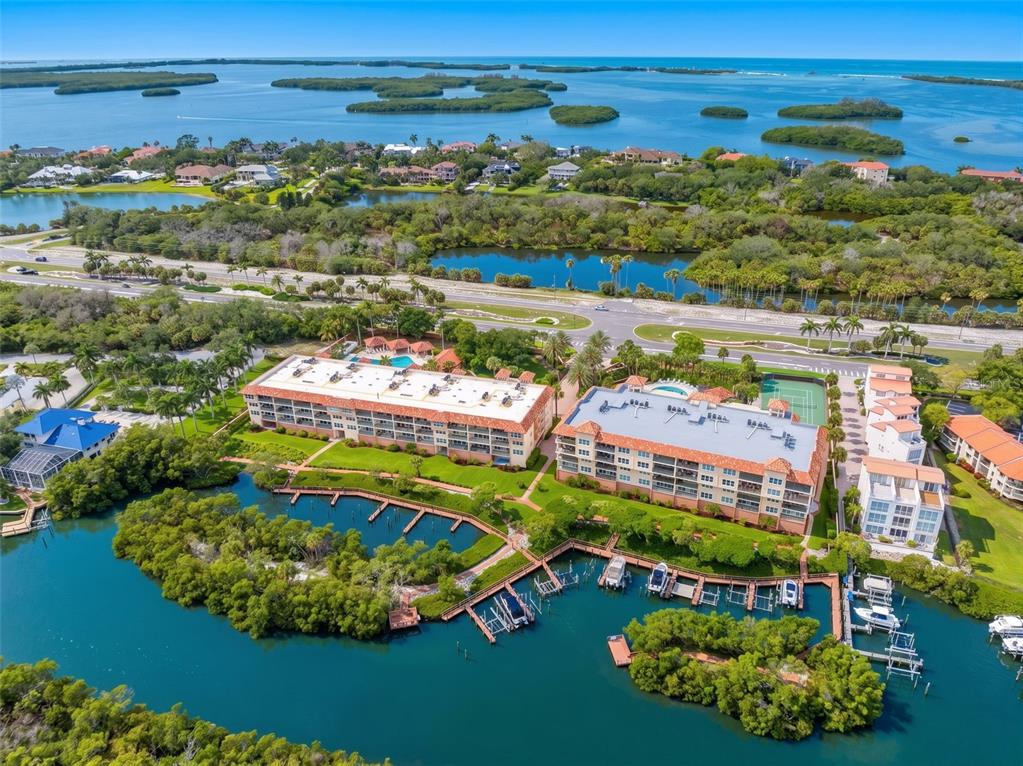 An aerial view shows two multi-story apartment buildings with pools and docks along a waterway — 1695 PINELLAS BAYWAY S UNIT D1, TIERRA VERDE, FL