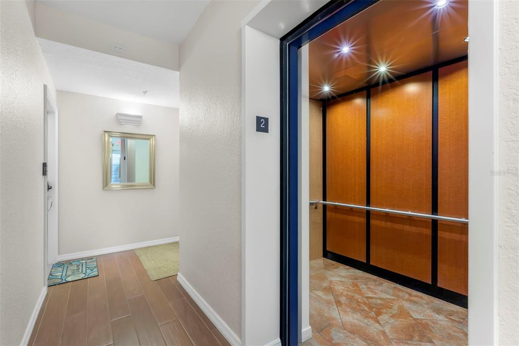 An elevator with wood-paneled walls opens into a hallway with tile flooring and a mirror — 1695 PINELLAS BAYWAY S UNIT D1, TIERRA VERDE, FL