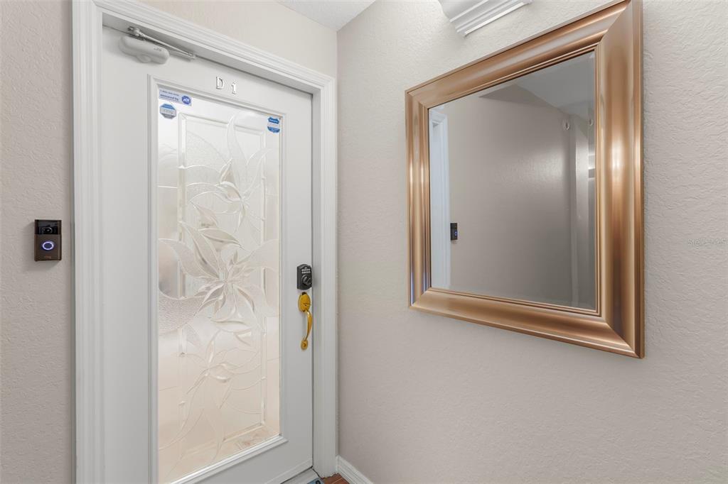 A white front door with a decorative glass insert sits beside a large gold-framed mirror — 1695 PINELLAS BAYWAY S UNIT D1, TIERRA VERDE, FL