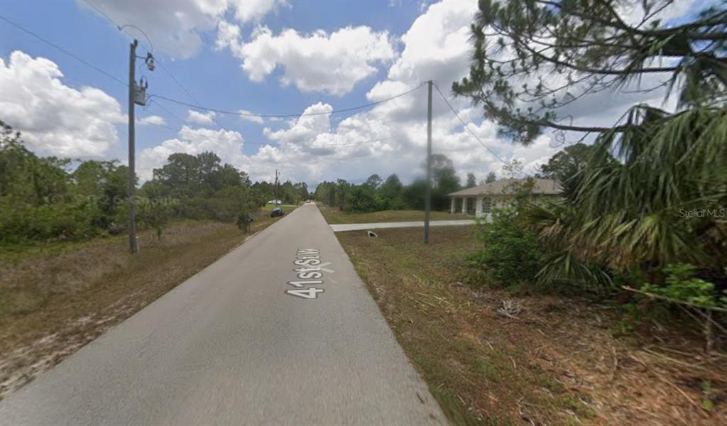 A paved road stretches through a rural area with trees and a house nearby — 3209 41ST STREET W, LEHIGH ACRES, FL