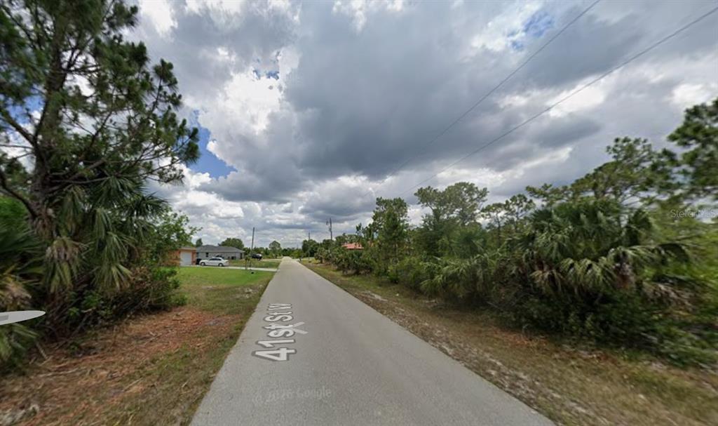 A paved road runs through a residential area with trees and shrubs on both sides — 3209 41ST STREET W, LEHIGH ACRES, FL
