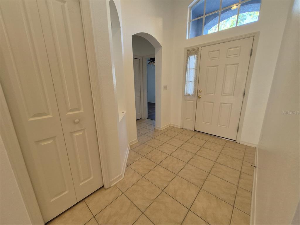 An entryway with beige tile flooring, a white front door, and an arched hallway — 6833 RUNNER OAK DRIVE, ZEPHYRHILLS, FL
