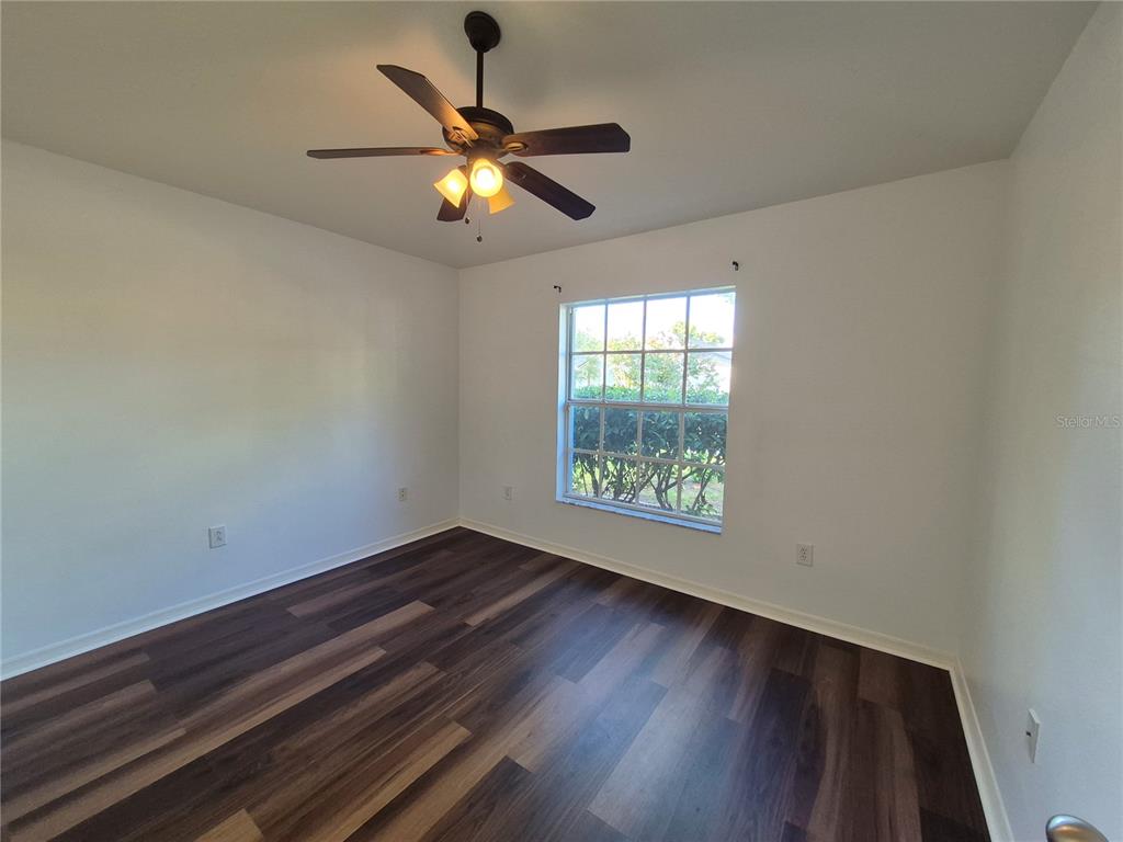 An empty bedroom features white walls, dark wood-look flooring, a ceiling fan, and a window — 6833 RUNNER OAK DRIVE, ZEPHYRHILLS, FL