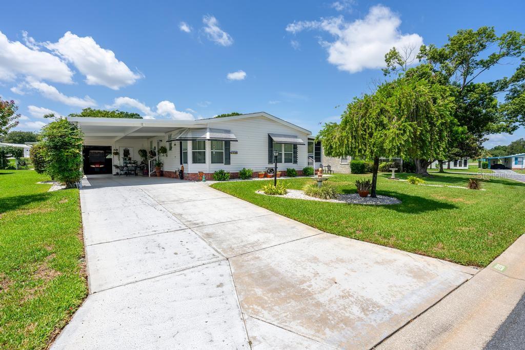 A white single-story manufactured home features a concrete driveway, a carport, and a landscaped lawn — 1226 POMPANO LANE, LADY LAKE, FL