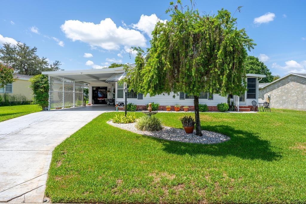 A white single-story house with a carport and a large weeping tree in the yard — 1226 POMPANO LANE, LADY LAKE, FL