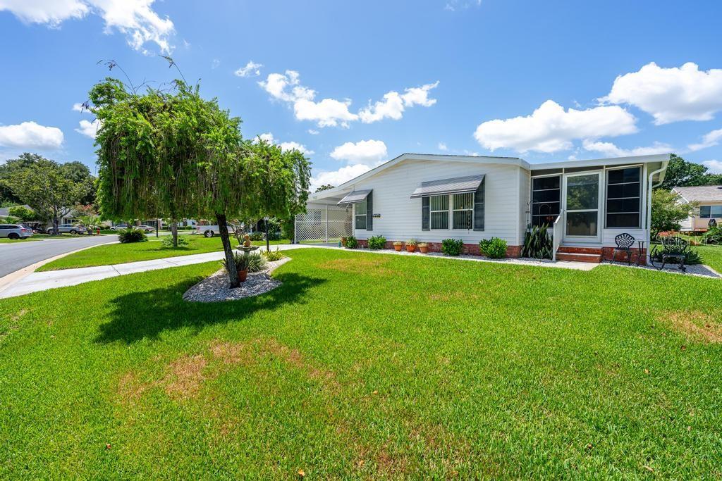 A white single-story house with a carport and a large green lawn — 1226 POMPANO LANE, LADY LAKE, FL