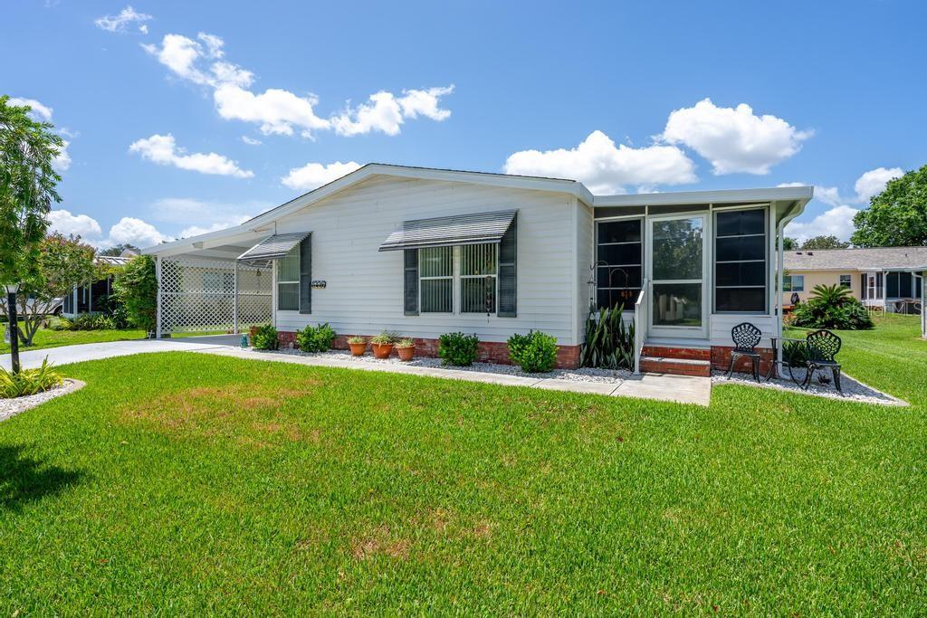 A single-story manufactured home with white siding, a carport, and a screened-in front porch — 1226 POMPANO LANE, LADY LAKE, FL