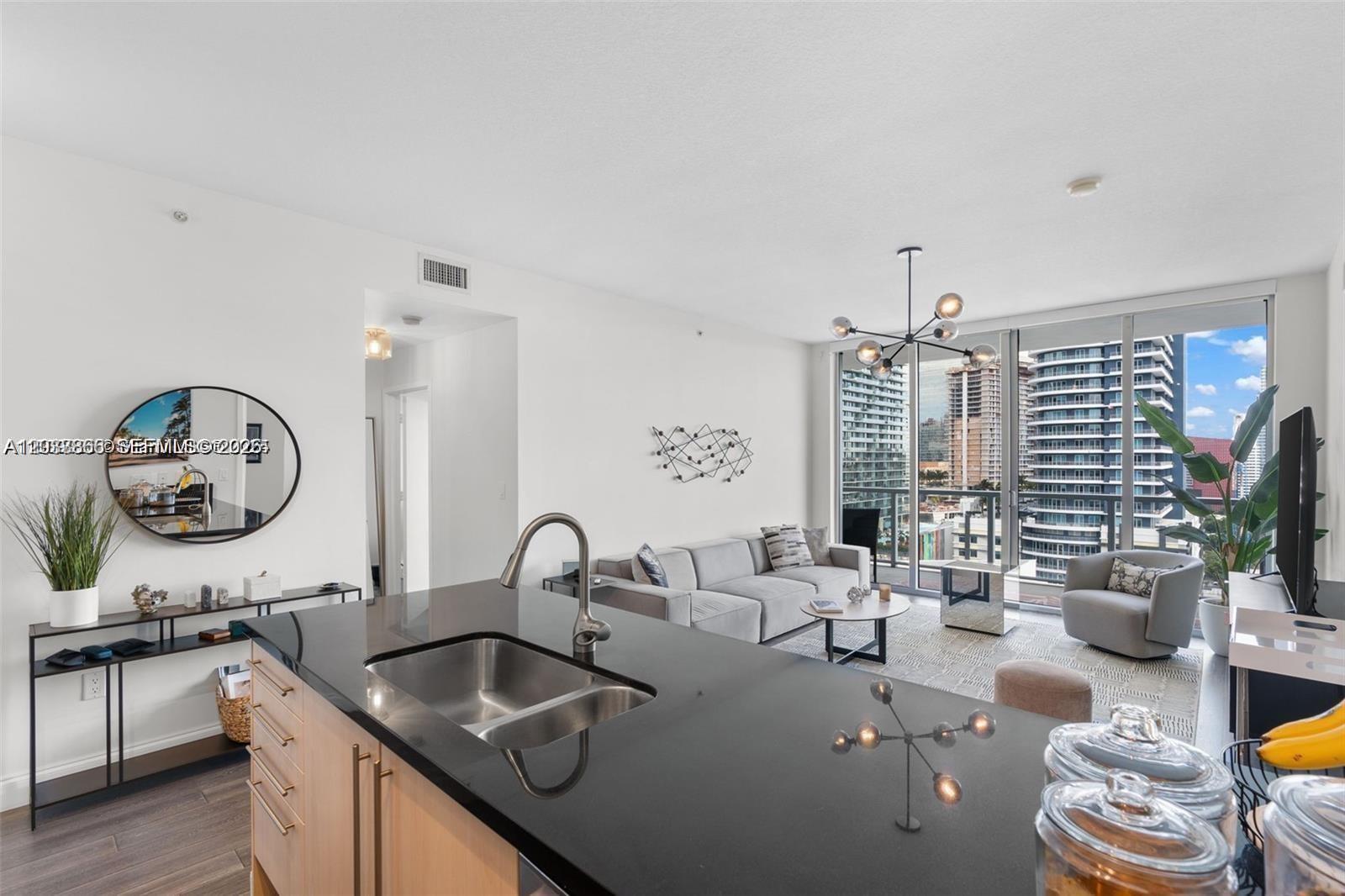 A modern kitchen island overlooks a living room with floor-to-ceiling windows and city views — 79 SW 12th St, Miami FL 33130, MIAMI, FL