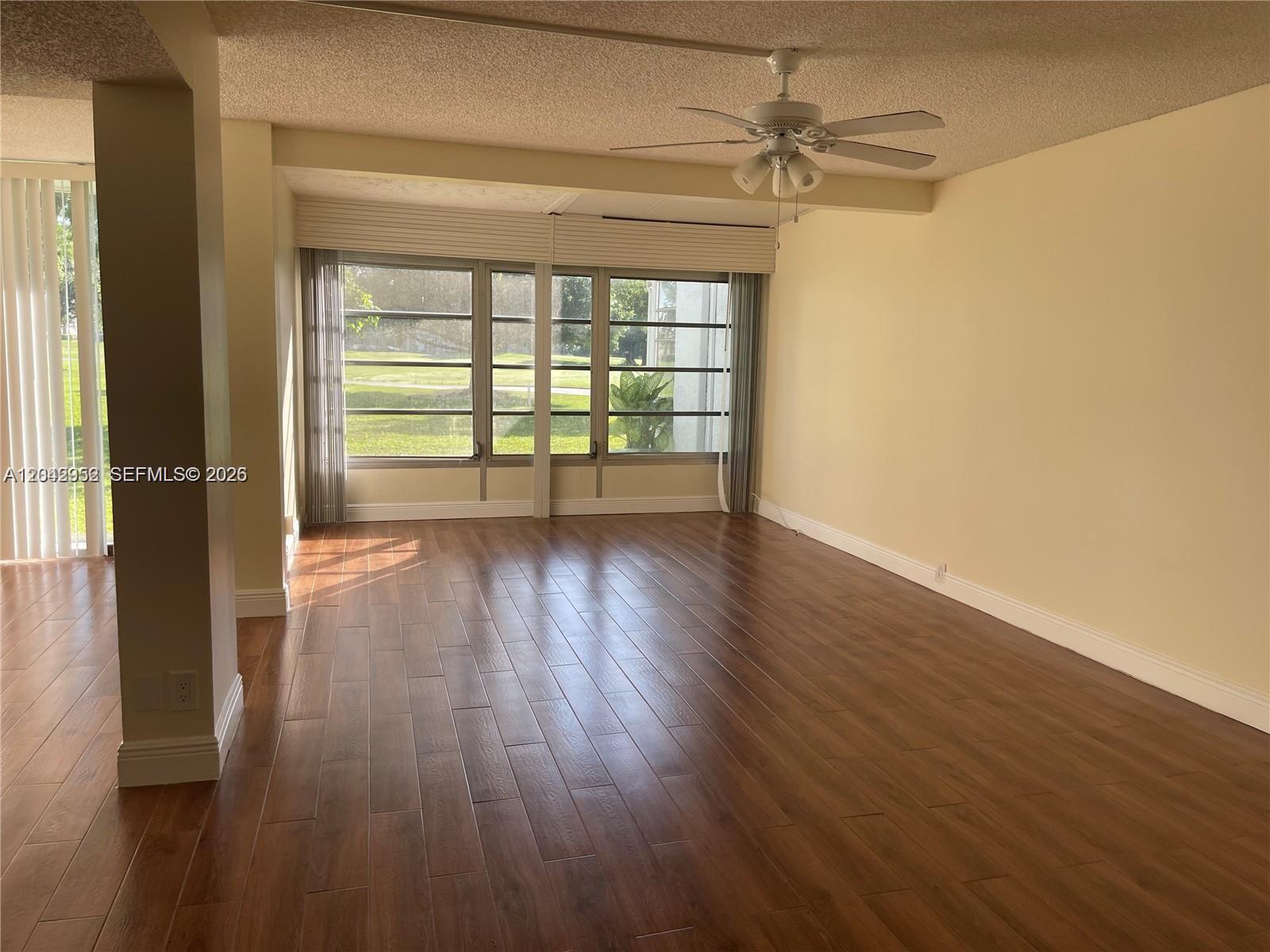 An empty living room features wood-look flooring, a ceiling fan, and large windows overlooking grass — 9401 Evergreen Pl # 103, Davie FL 33324, DAVIE, FL