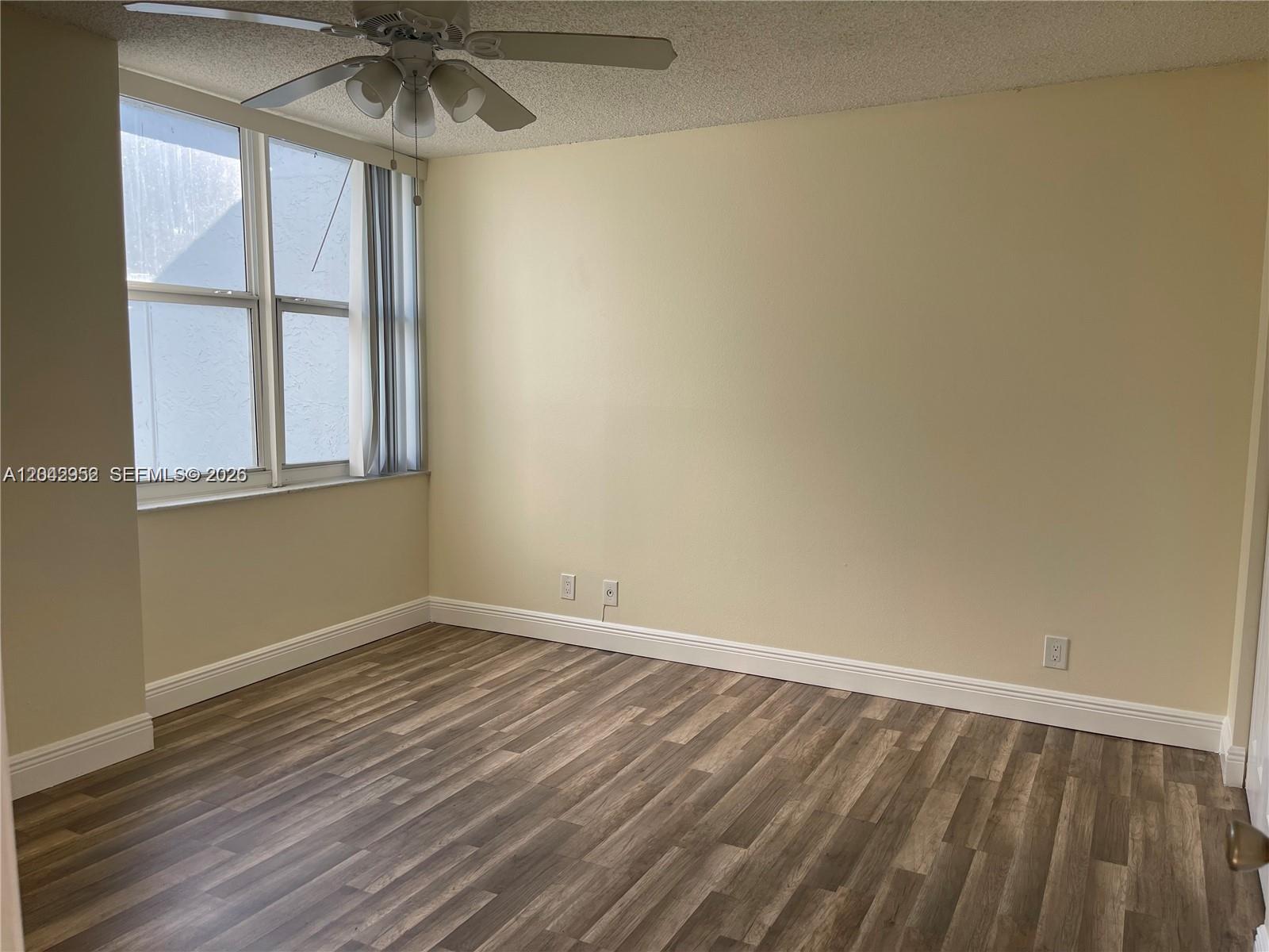 An empty room features light-colored walls, wood-look flooring, a ceiling fan, and a large window — 9401 Evergreen Pl # 103, Davie FL 33324, DAVIE, FL