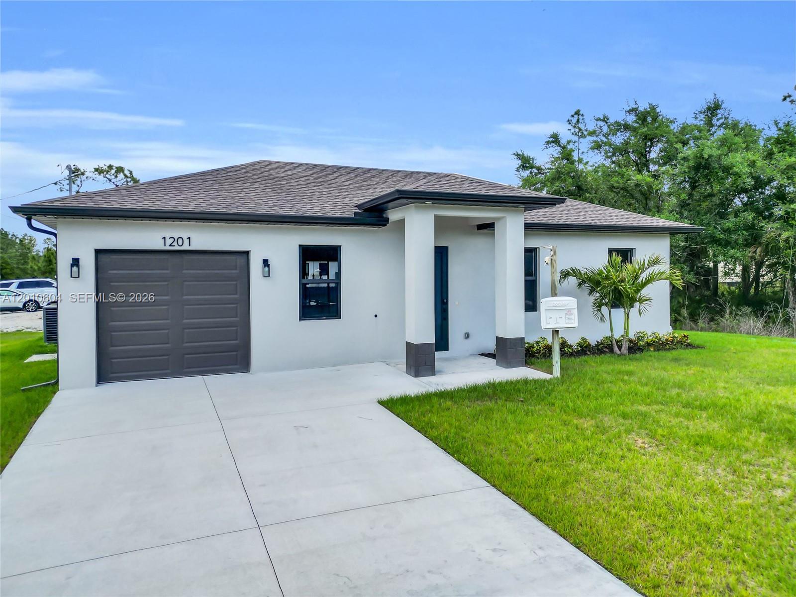 A single-story house with a gray garage door, white stucco exterior, and a concrete driveway — 1201 E 7th ST, Lehigh Acres FL 33972, LEHIGH ACRES, FL