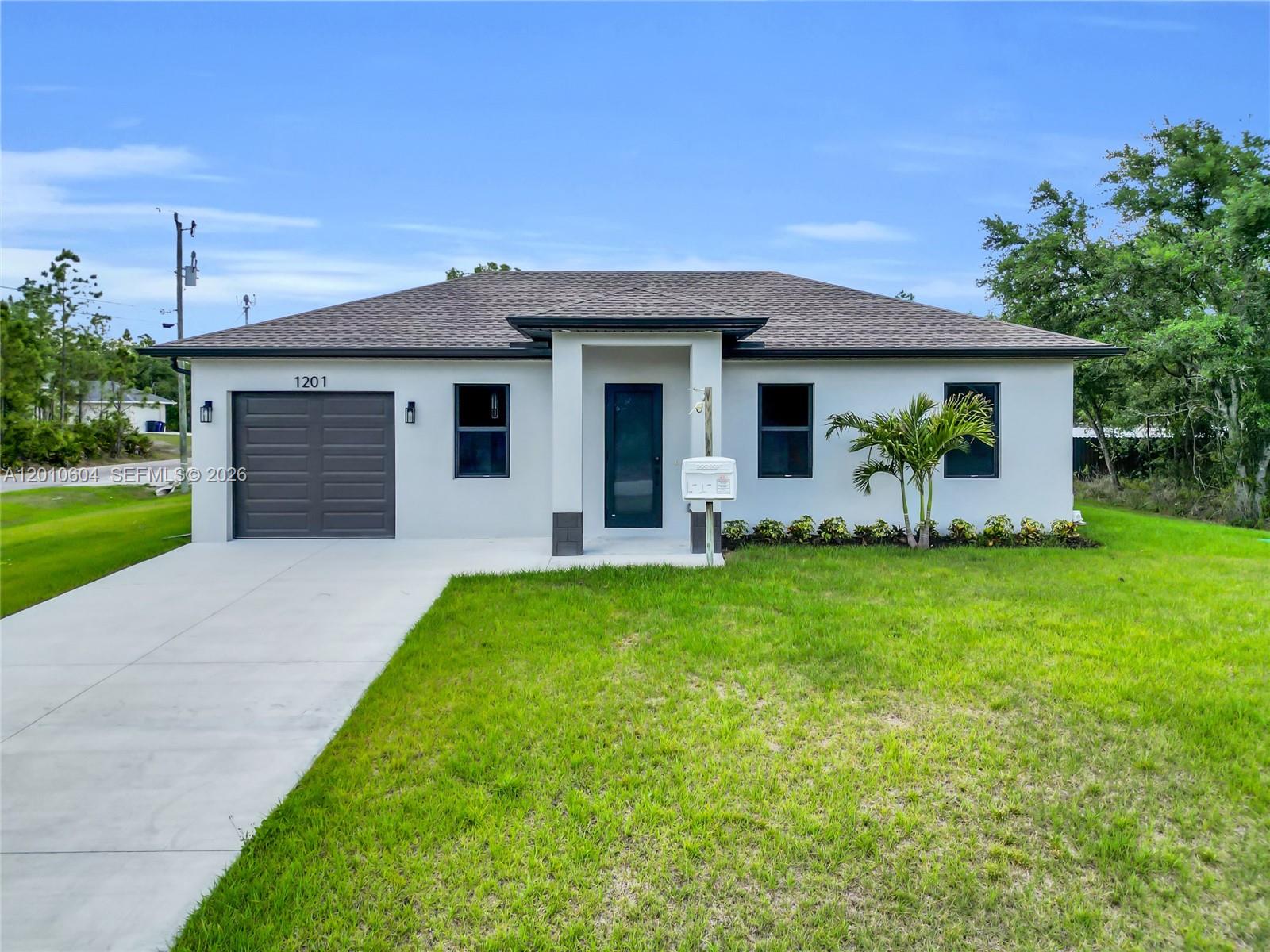 A single-story house with a white exterior, dark garage door, and a front lawn — 1201 E 7th ST, Lehigh Acres FL 33972, LEHIGH ACRES, FL