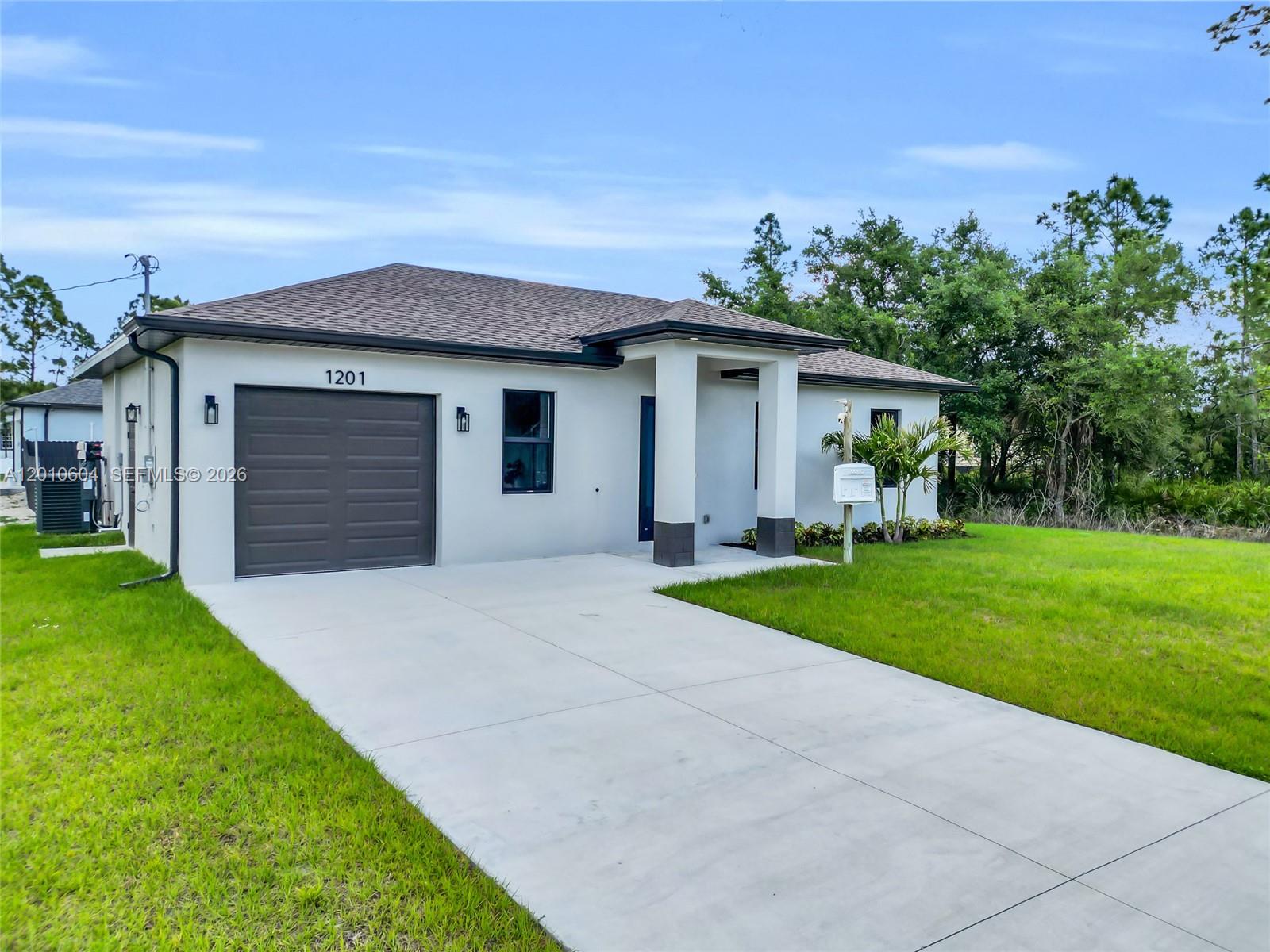 A single-story house with a white stucco exterior, a dark garage door, and a concrete driveway — 1201 E 7th ST, Lehigh Acres FL 33972, LEHIGH ACRES, FL