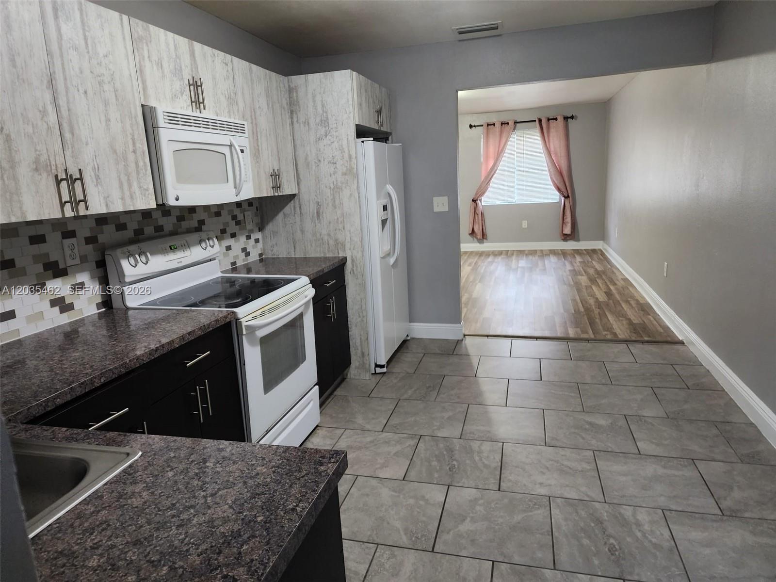 A kitchen with dark lower cabinets, light wood-grain upper cabinets, and a view into a room — 13963 NE 3rd Ct # D2, North Miami FL 33161, NORTH MIAMI, FL