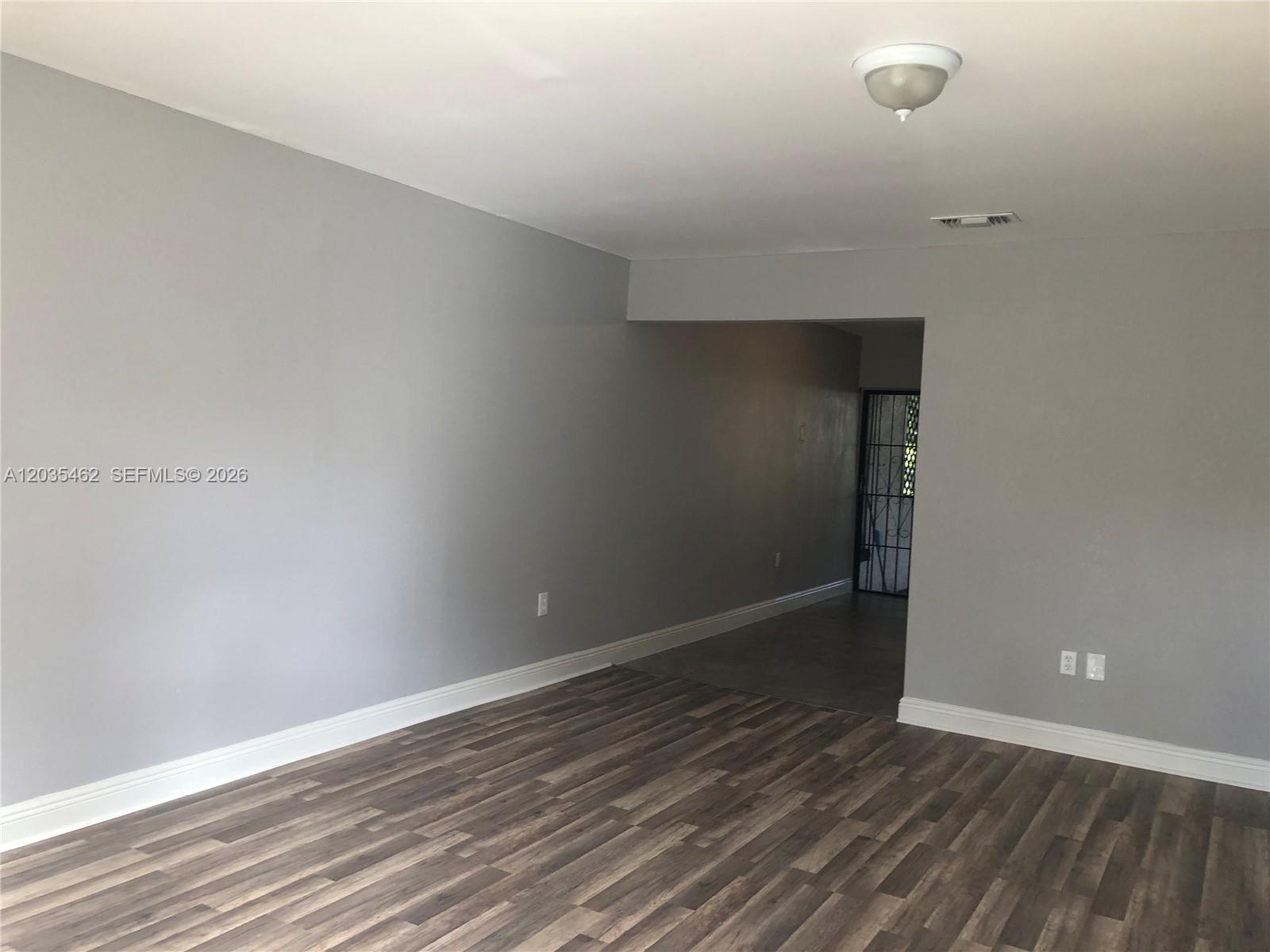 An empty room features gray walls, wood-look flooring, white baseboards, and a ceiling light fixture — 13963 NE 3rd Ct # D2, North Miami FL 33161, NORTH MIAMI, FL