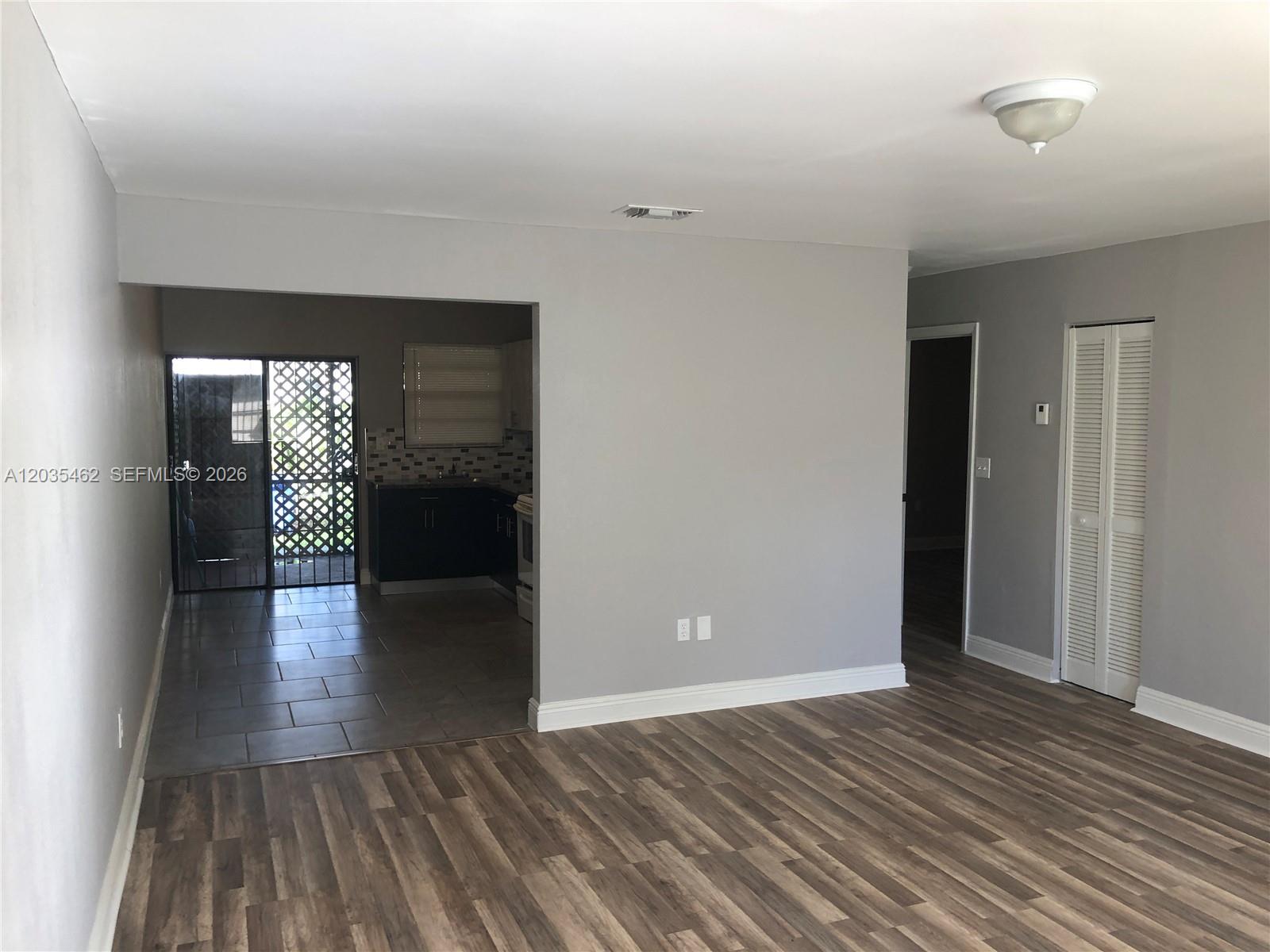 A living room with wood-look flooring leads to a tiled kitchen and a sliding door — 13963 NE 3rd Ct # D2, North Miami FL 33161, NORTH MIAMI, FL