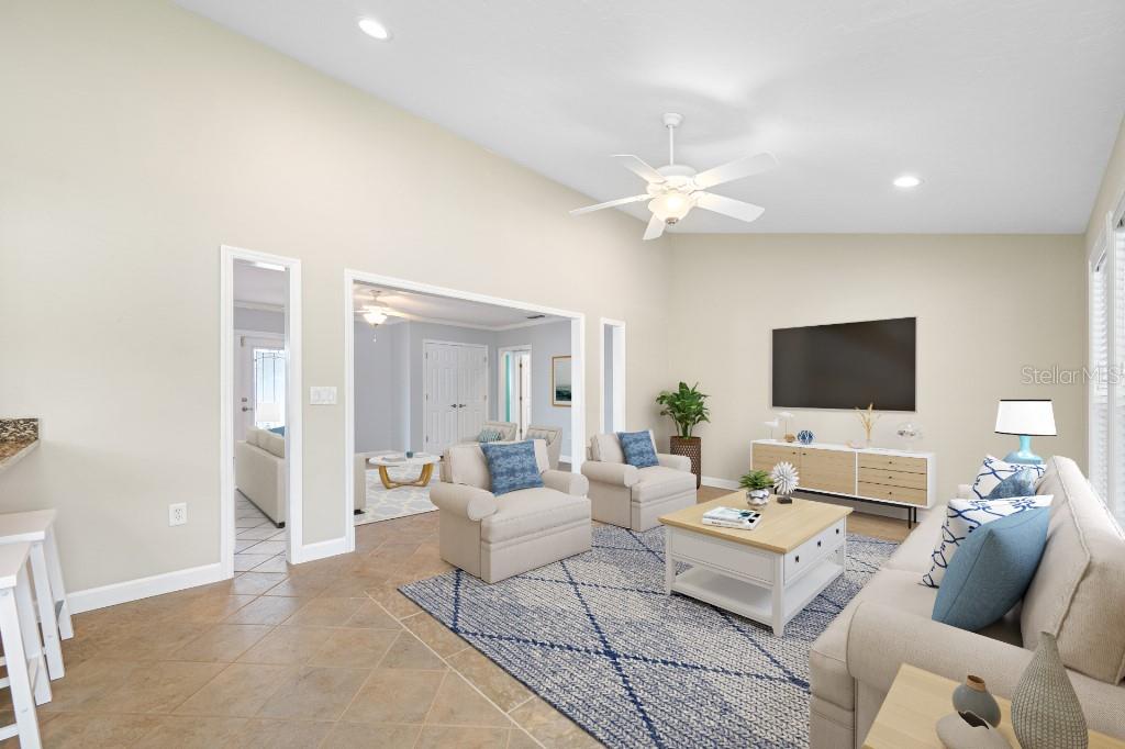 A living room with vaulted ceilings, tile floors, a blue area rug, and neutral furniture — 10308 SANDPIPER ROAD W, BRADENTON, FL
