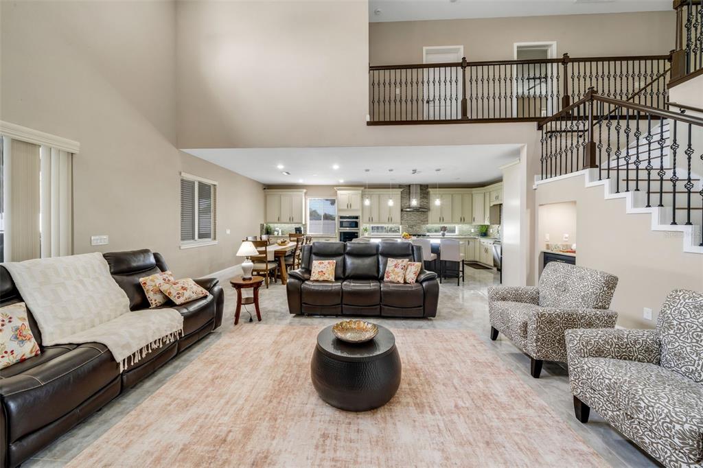 A spacious open-concept living room features a high ceiling, dark leather furniture, and a kitchen — 545 GANDHI DRIVE, LAKELAND, FL