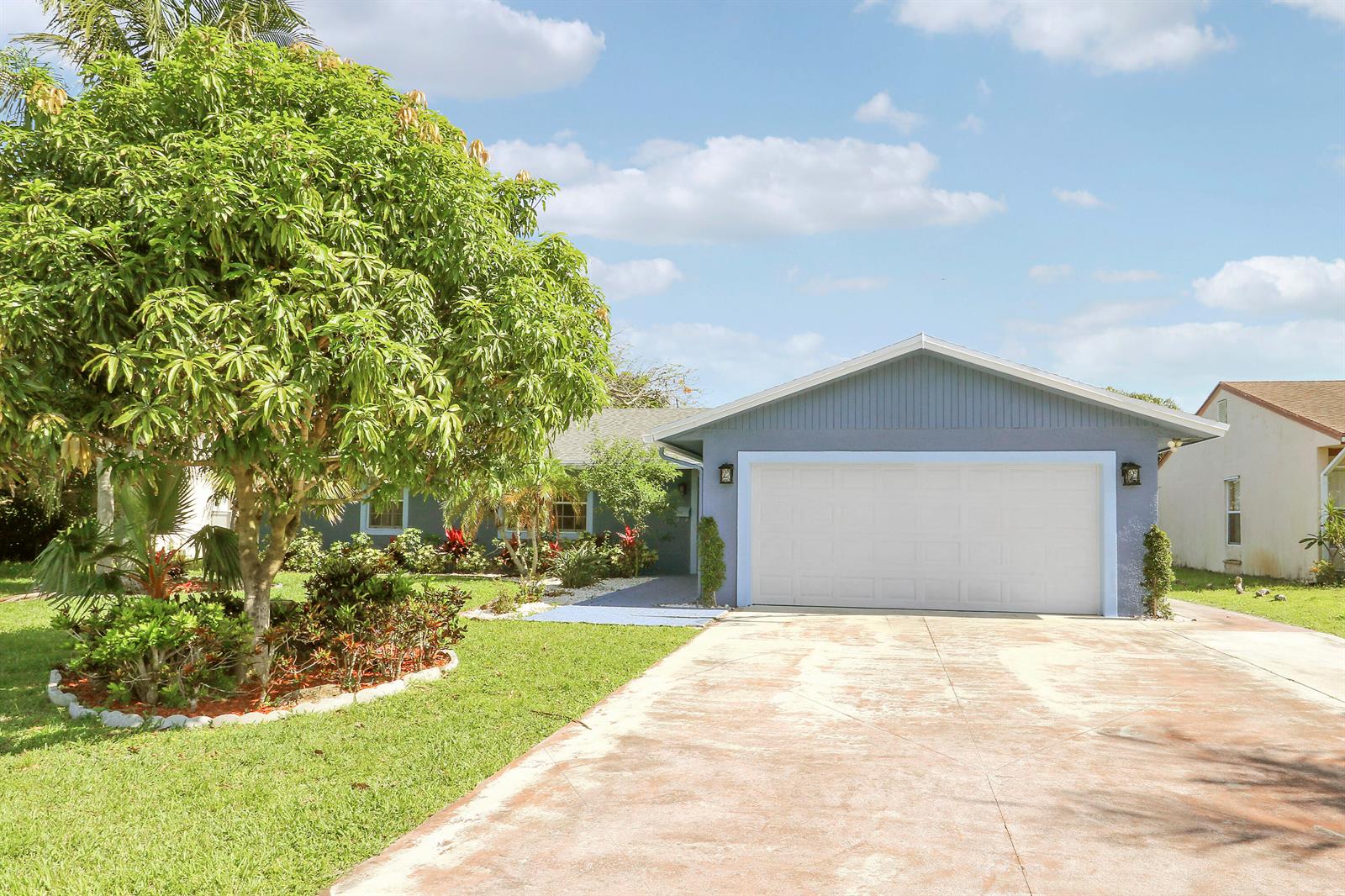 A blue single-story house features a two-car garage, a concrete driveway, and a large tree — 3336 Ave Villandry, Delray Beach FL 33445, DELRAY BEACH, FL